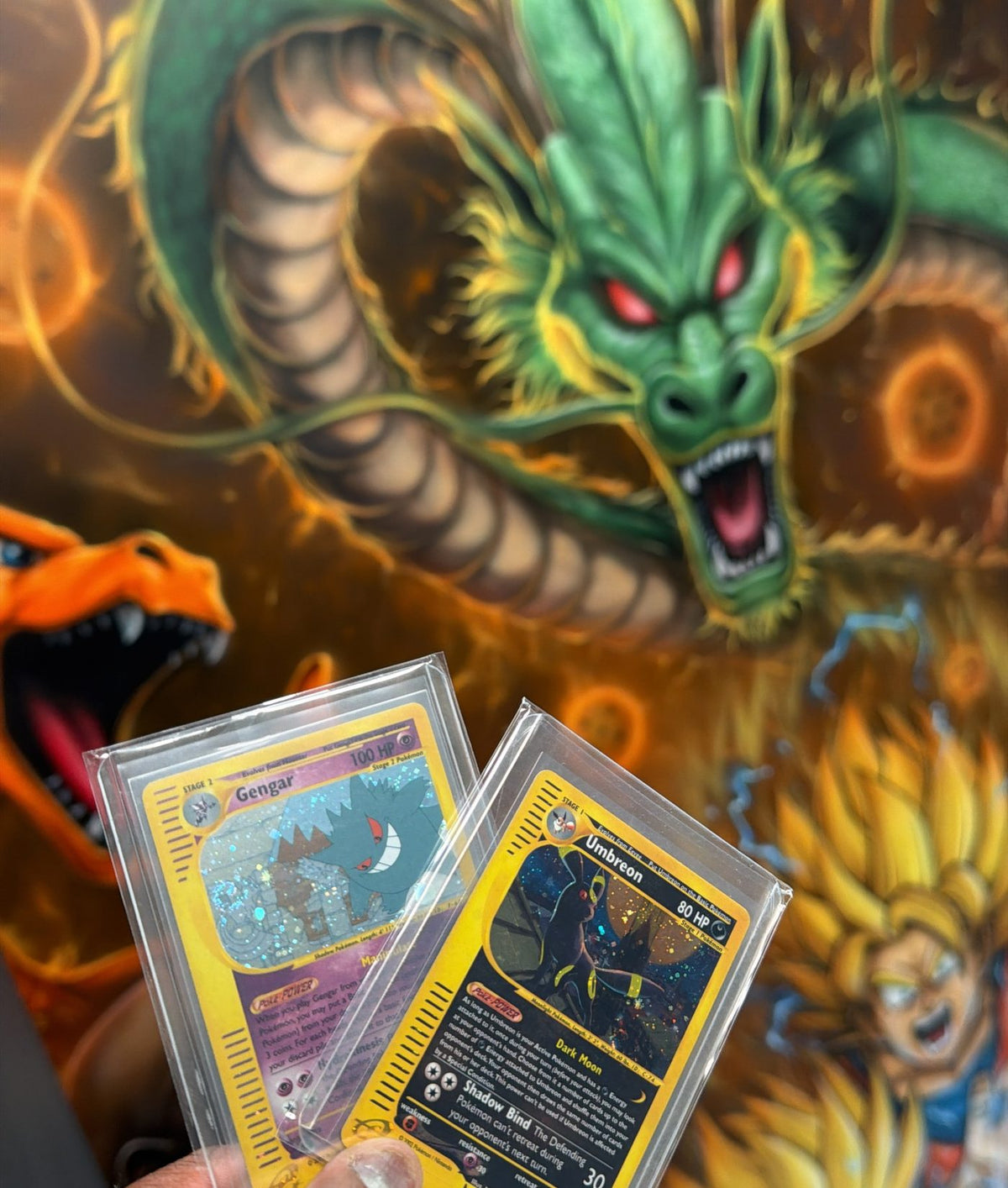 Holo Gengar and Umbreon cards held up in front of a Pokémon and dragon mural